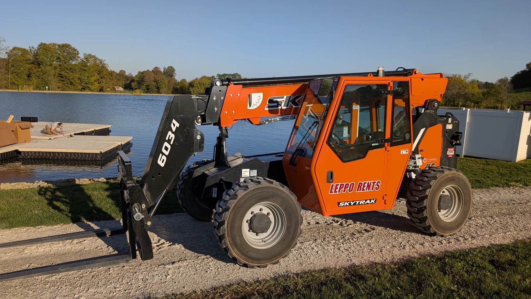The telehandler beside the pond while dock sections are assembled on the water.