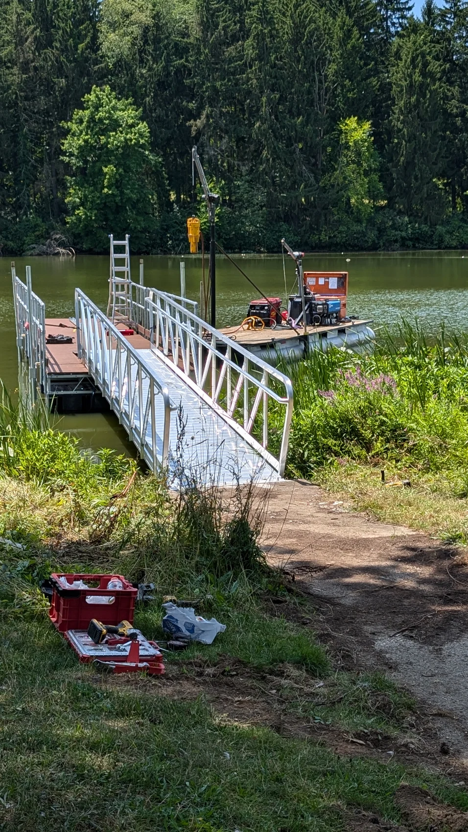 The gangway extending from the bank toward the floating fishing pier during installation.