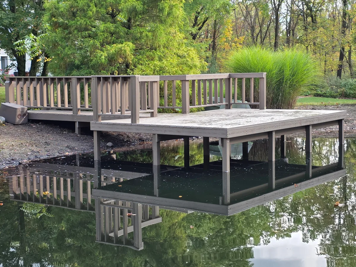 Finished fixed pond dock supported by posts with a connected shore platform and railing