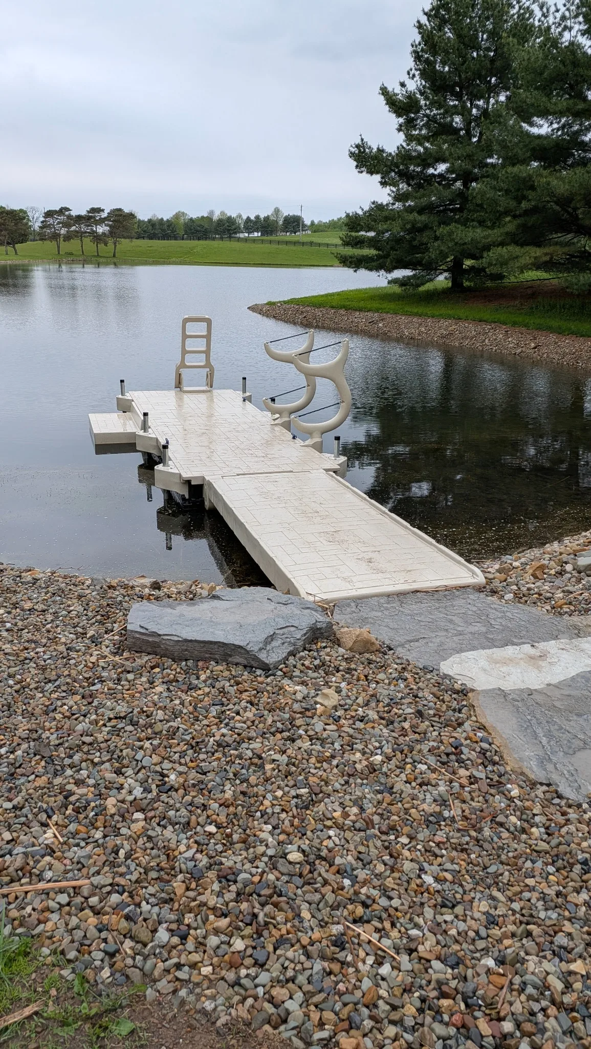 Stone shoreline approach leading to a floating pond dock with kayak storage