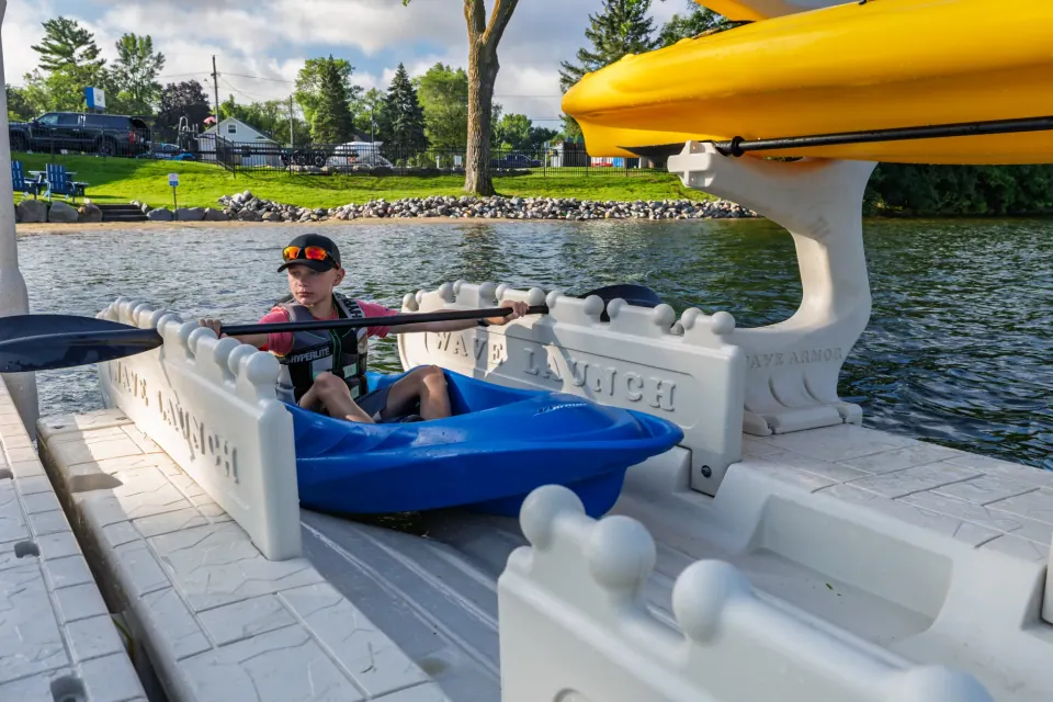 A paddler wearing a life jacket seated in a kayak between the launch hand-grip rails.